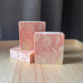 Three pink soap bars with a wavy pattern on a wooden surface.