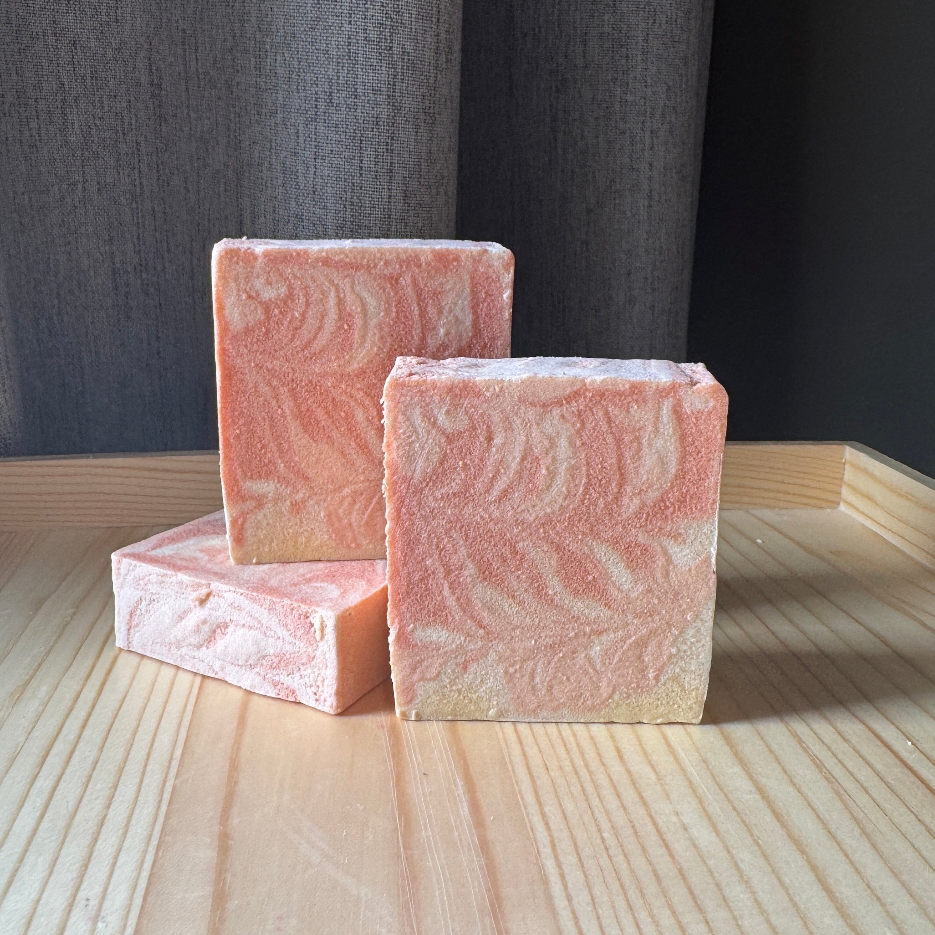 Three pink soap bars with a wavy pattern on a wooden surface.