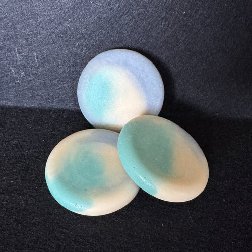 Three oval soap bars with a marbled pattern of light blue, mint green, and cream, arranged on a dark textured background.