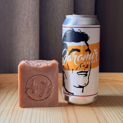 Bar of soap next to a can of beer on a wooden surface