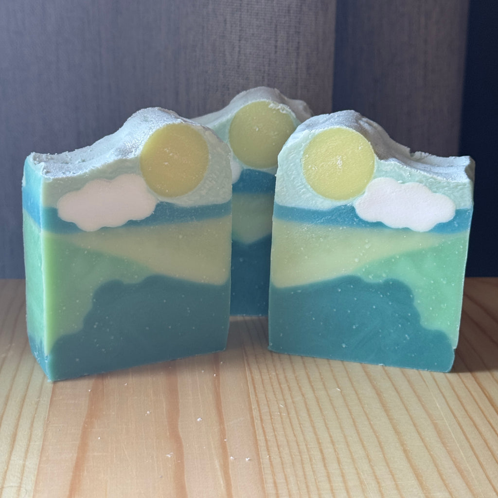 Two bars of soap with a landscape design on a wooden surface