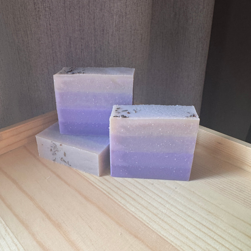 Three layered soap bars with a gradient of purple and white on a wooden surface.