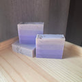 Three layered soap bars with a gradient of purple and white on a wooden surface.
