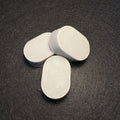 Three oval light purple soaps arranged on a dark textured background.