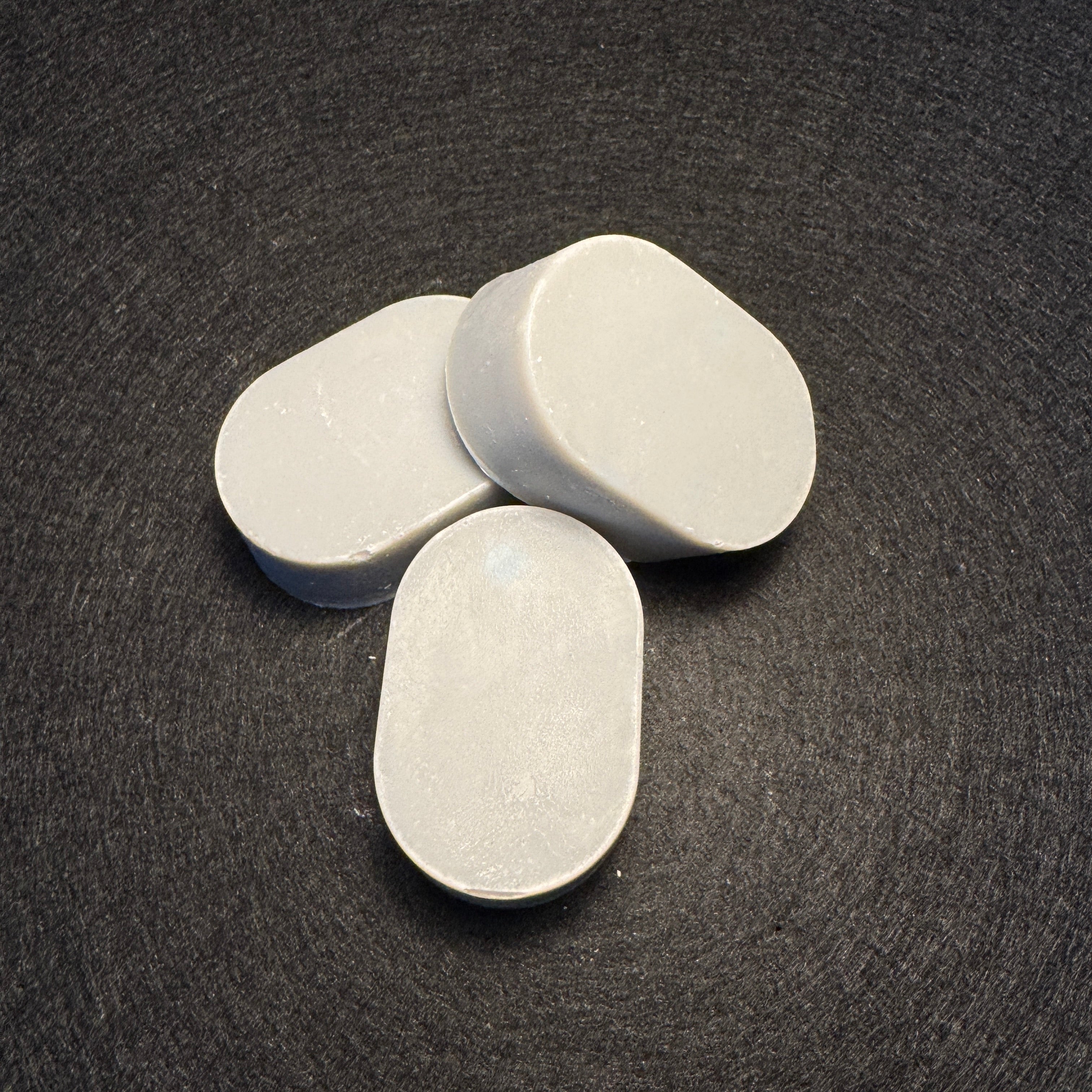 Three oval light purple soaps arranged on a dark textured background.