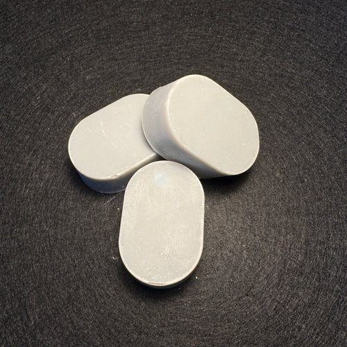 Three oval light purple soaps arranged on a dark textured background.