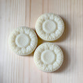 Three white textured soap bars on a light wooden surface