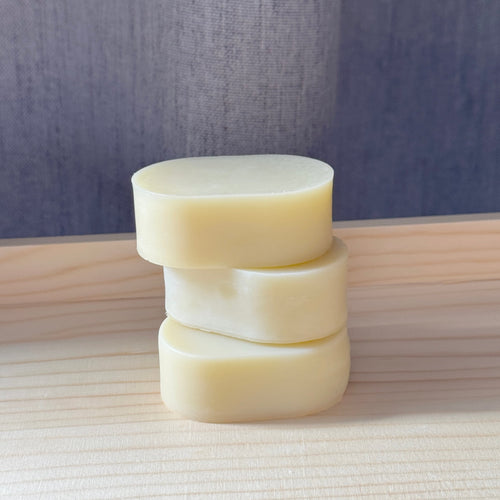 Stack of three cylindrical soap bars on a wooden surface with a neutral background