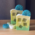 Three bars of soap with window-like cutouts and blue circular shapes on a wooden surface.