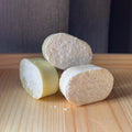 Three cylindrical soap bars of different colors on a wooden surface with a dark background