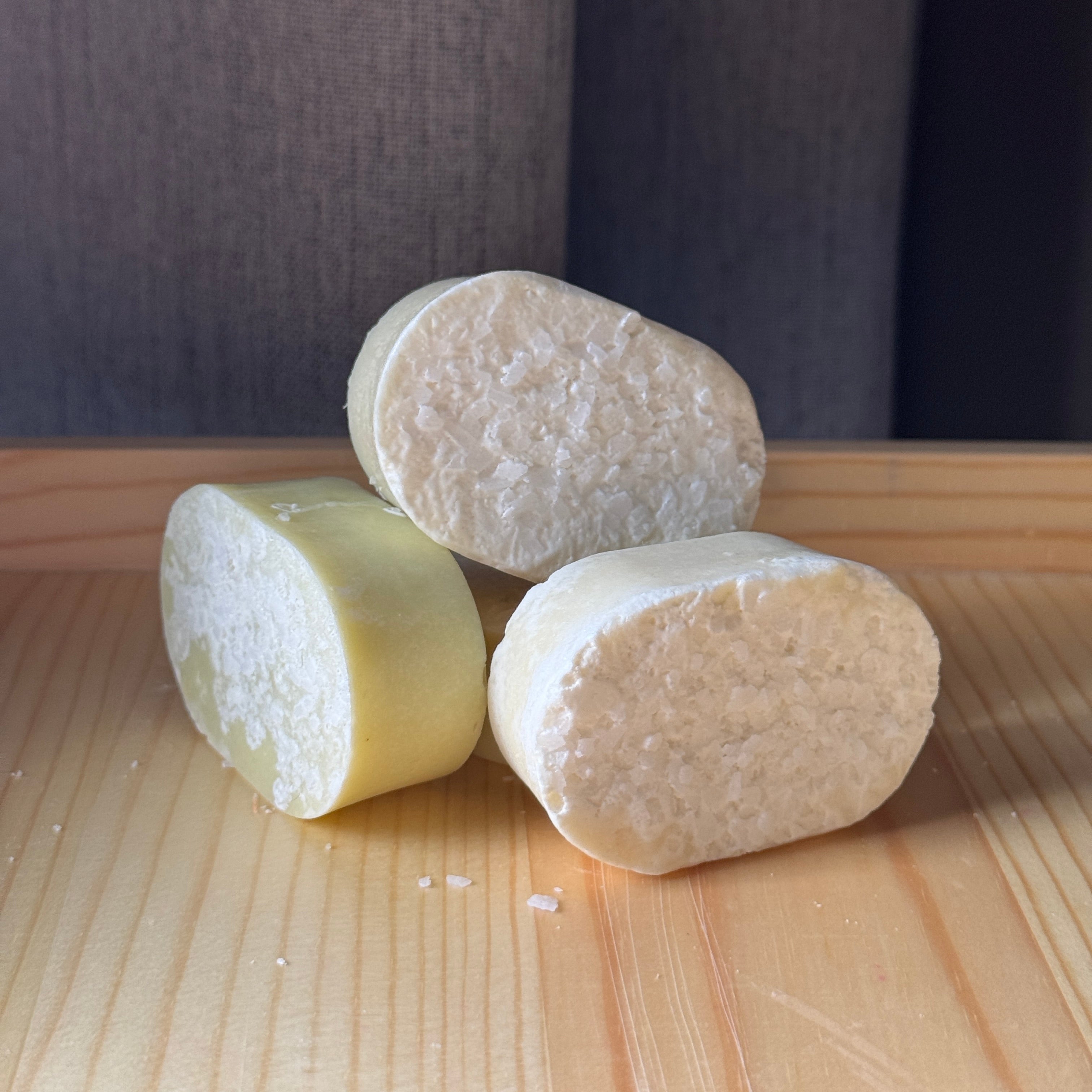 Three cylindrical soap bars of different colors on a wooden surface with a dark background