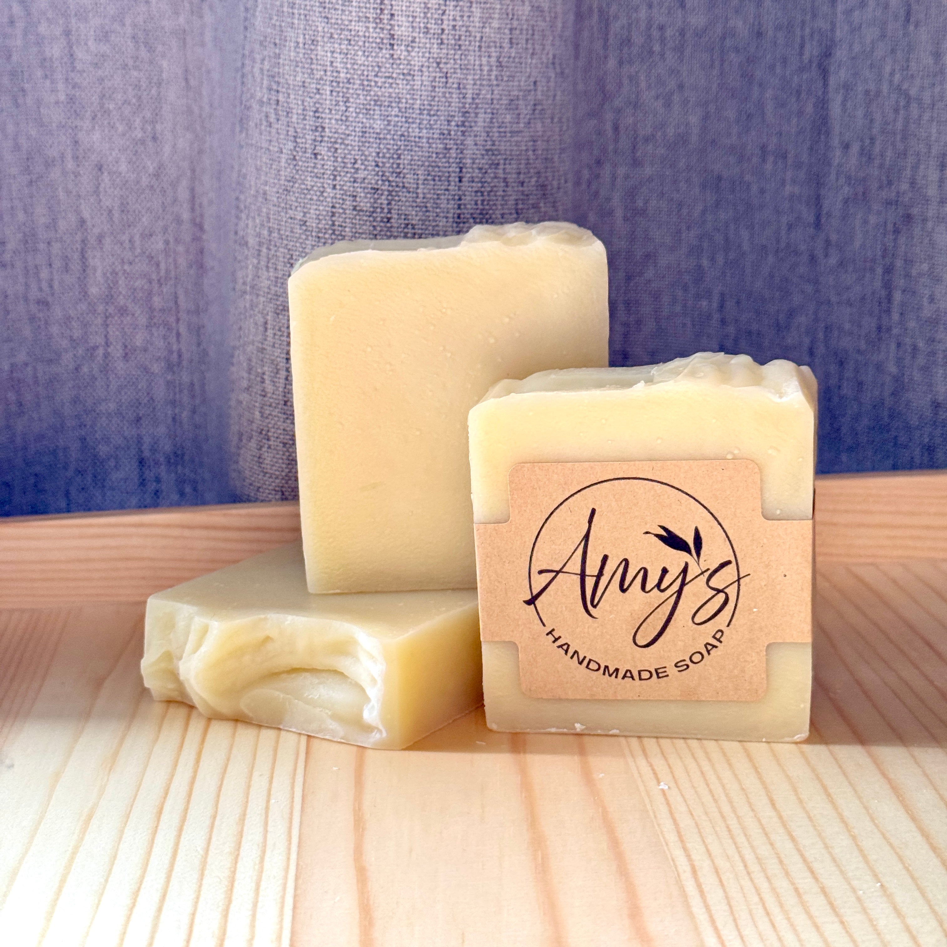 Three bars of handmade soap with a visible brand label on a wooden surface.