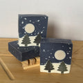 Three soap bars with winter scene designs on a wooden surface