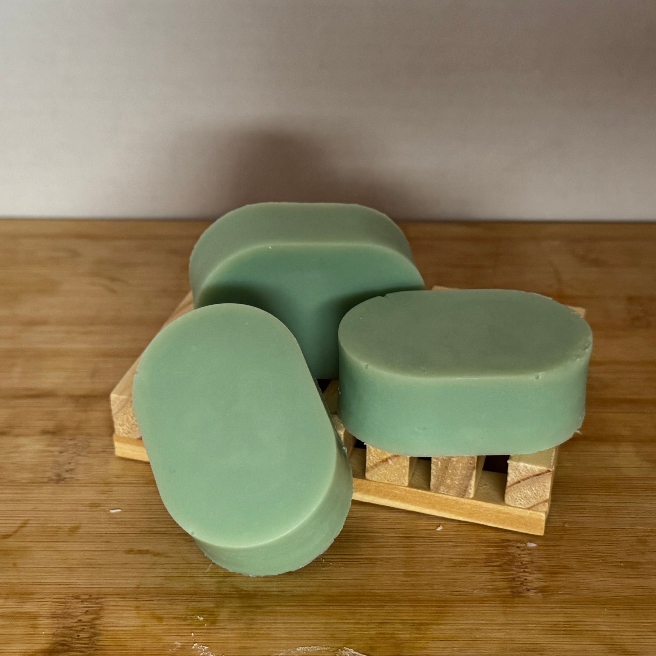 Three green soap bars on a wooden soap dish against a white wall.
