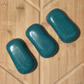 3 teal bars of oval shaped soap on a wooden board