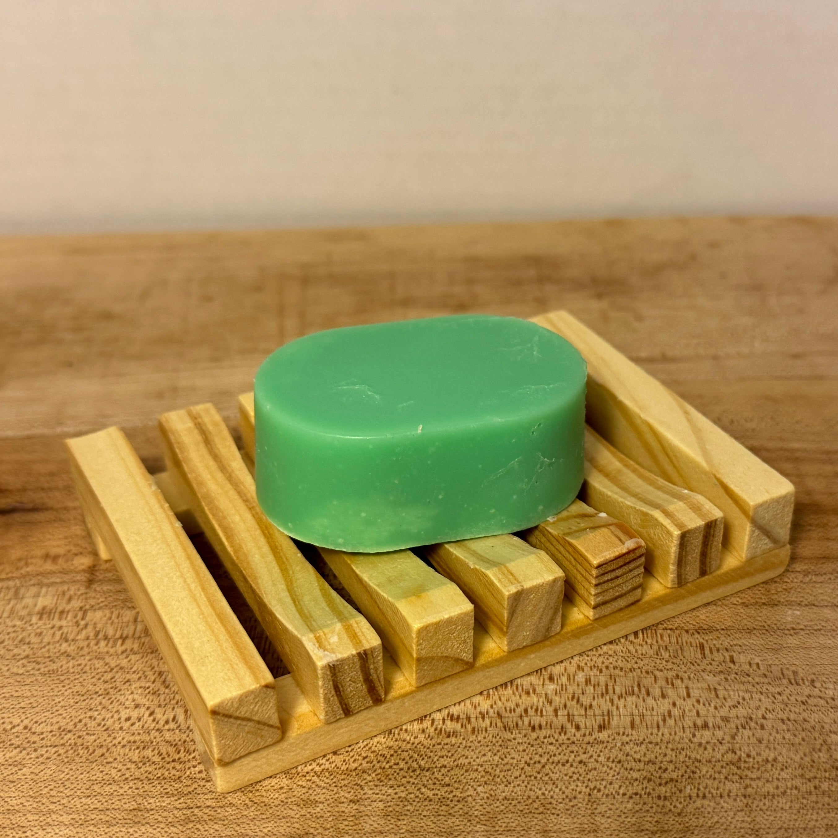 Green bar of soap on a wooden soap dish on a wooden surface.