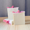 Three bars of soap with pink butterfly decorations on a wooden surface.