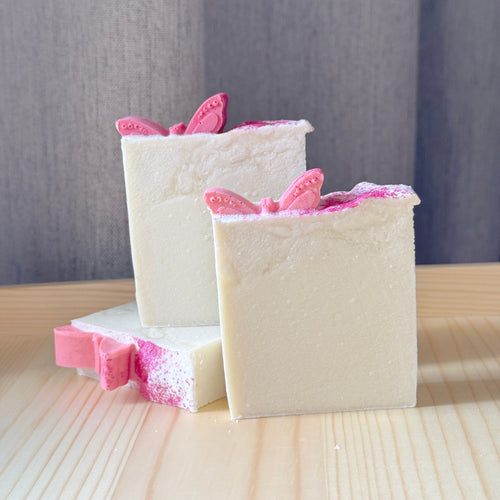 Three bars of soap with pink butterfly decorations on a wooden surface.