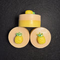 Three pineapple-themed soap bars arranged on a dark textured background, with one upright bar and two flat circular slices, each featuring a yellow pineapple detail on a beige base.