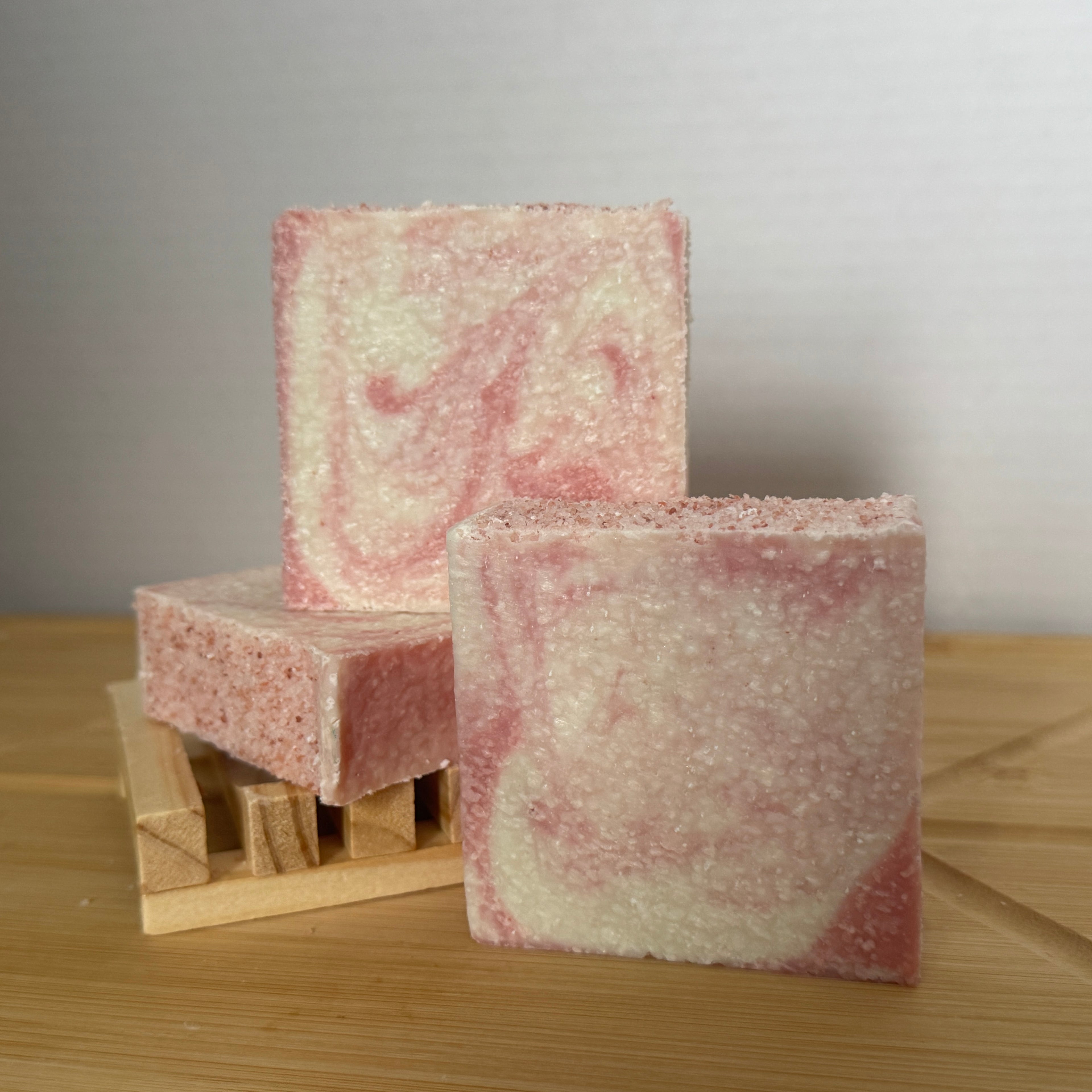 Two pink and white marbled soap bars on a wooden surface with a neutral background