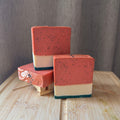 Three layered soap bars stacked on a wooden surface with a gray background