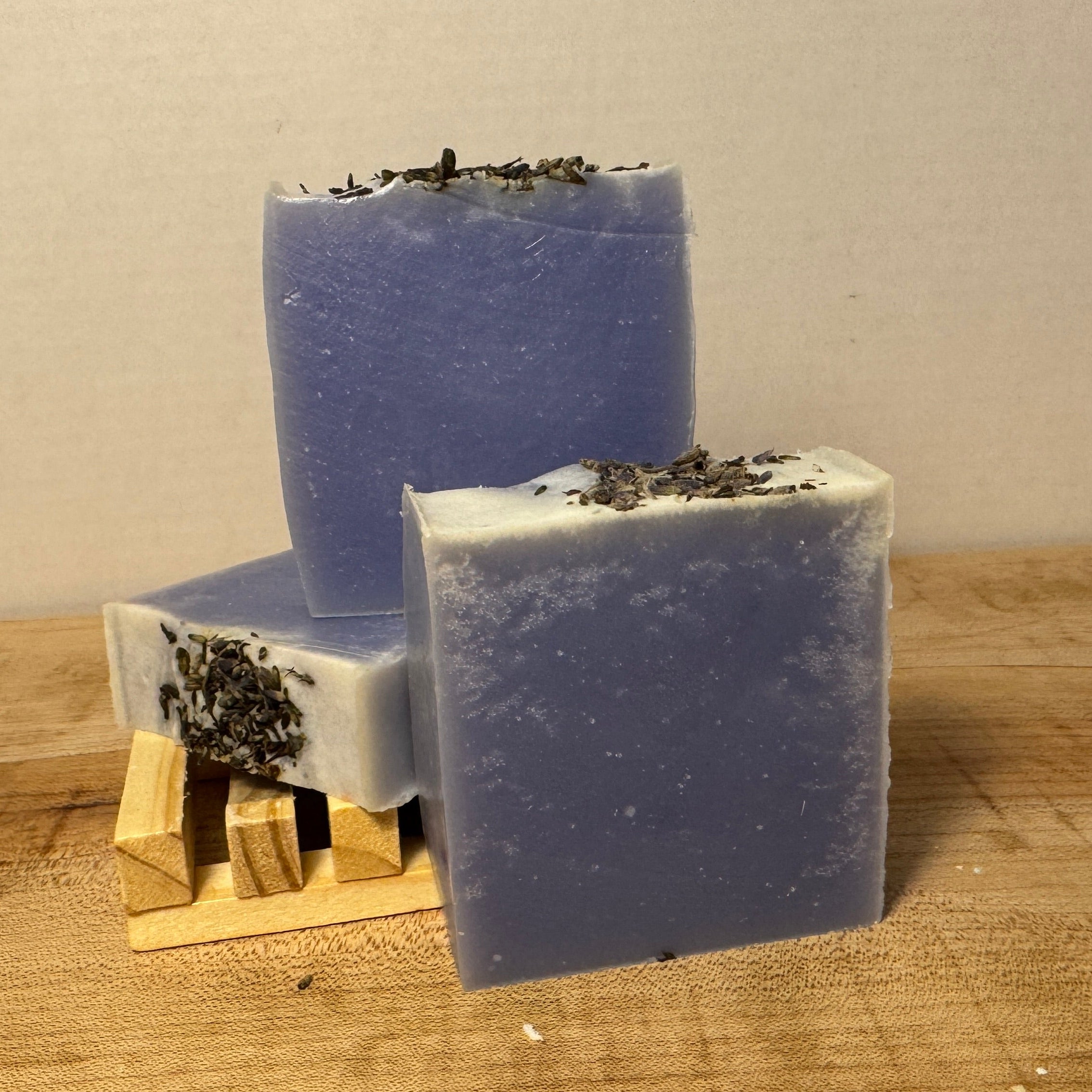 Three bars of blue soap with specks on a wooden surface