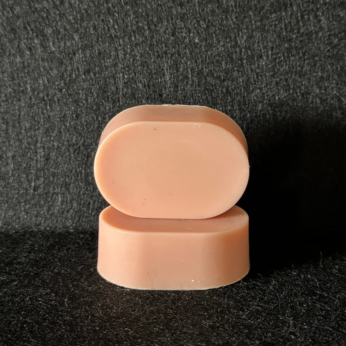 2 ovals of light pink soap stacked on a black felt surface