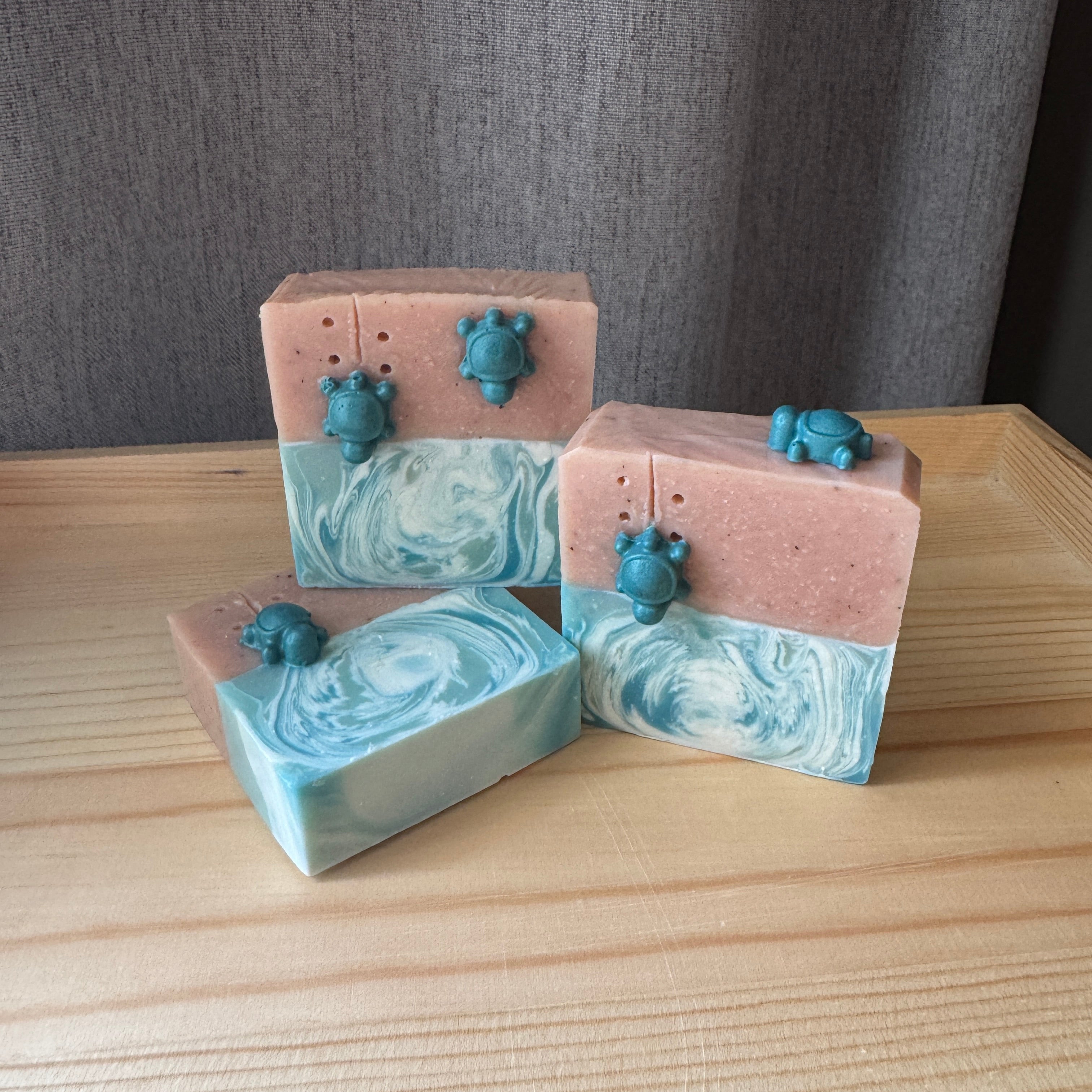 Three bars of soap with marbled design and turtle figurines on a wooden surface.