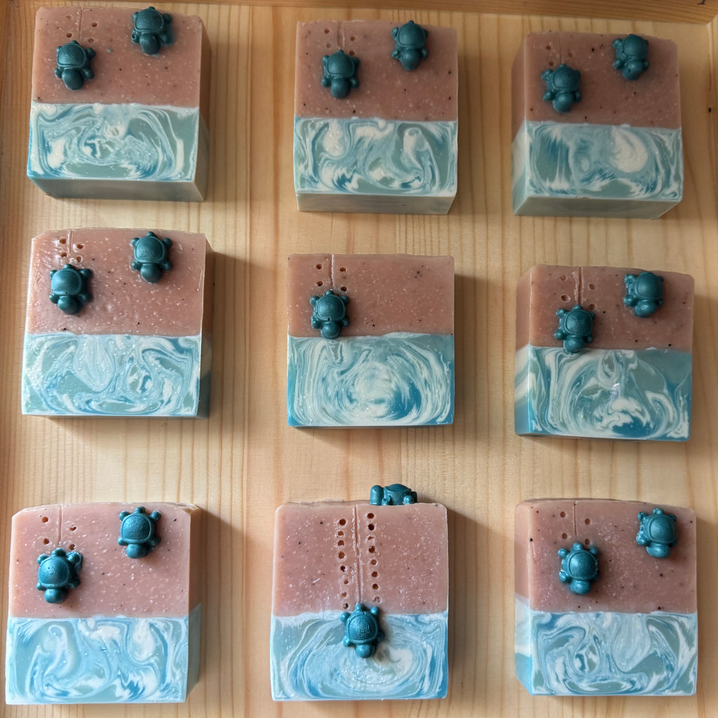 Nine square soap bars with marbled design and small figurines on a wooden surface