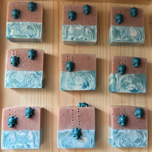 Nine square soap bars with marbled design and small figurines on a wooden surface