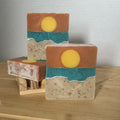 Three soap bars with artistic layered designs resembling a sea landscape on a wooden surface.