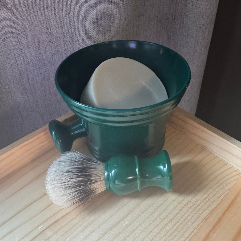 Green shaving brush and mug set on a wooden surface with a neutral background