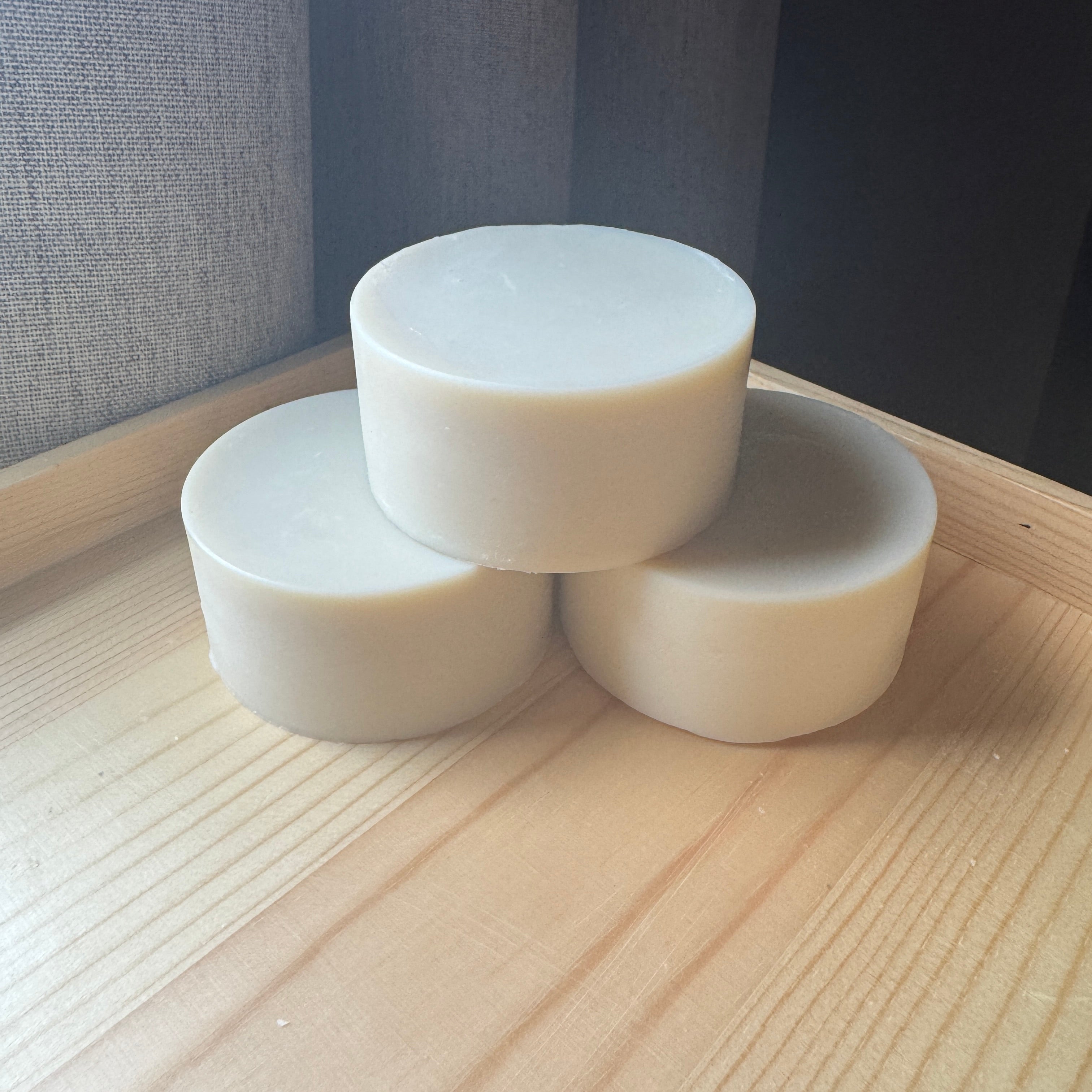 Three cylindrical white soaps stacked on a wooden surface with a neutral background