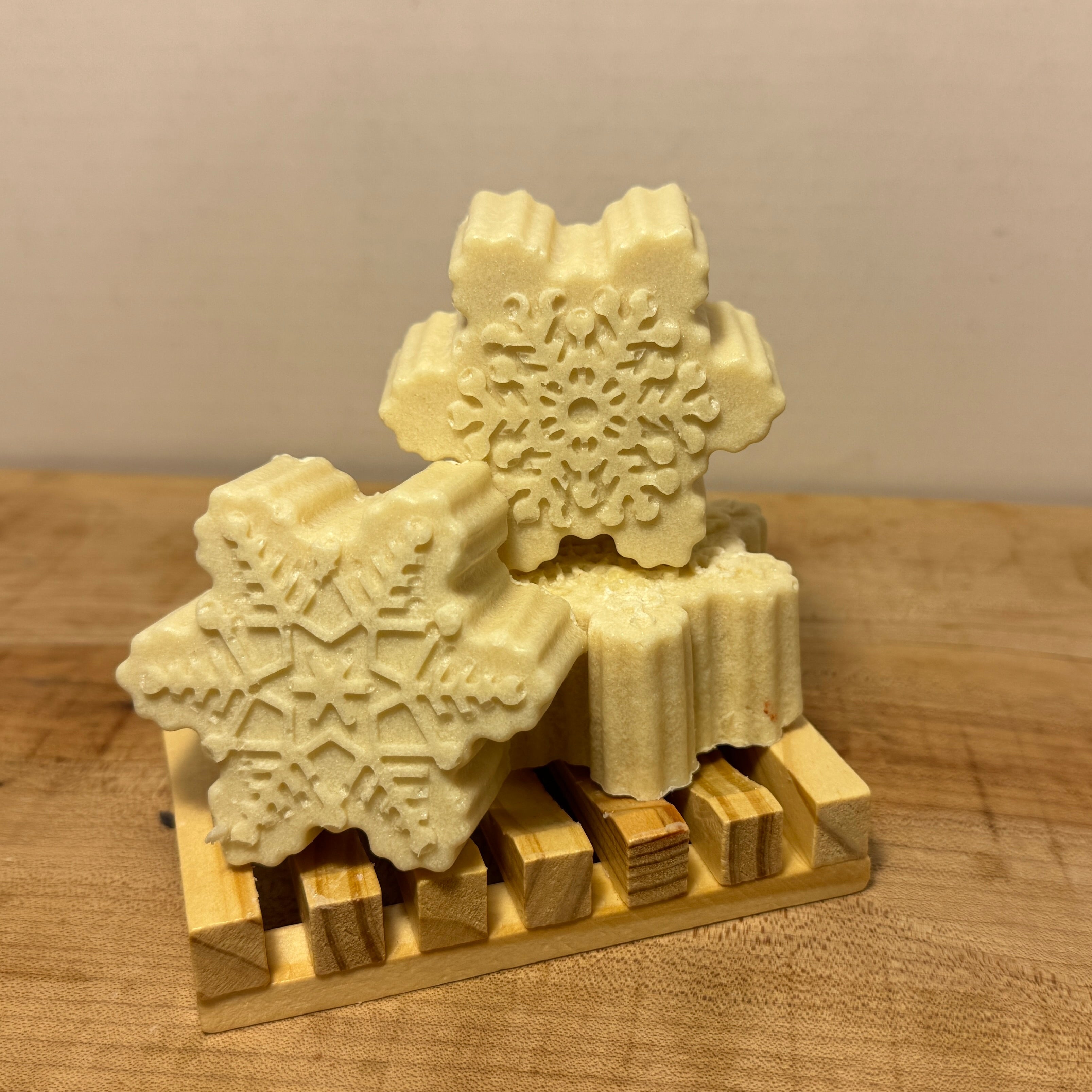 Snowflake-shaped soap bars on a wooden stand against a plain background