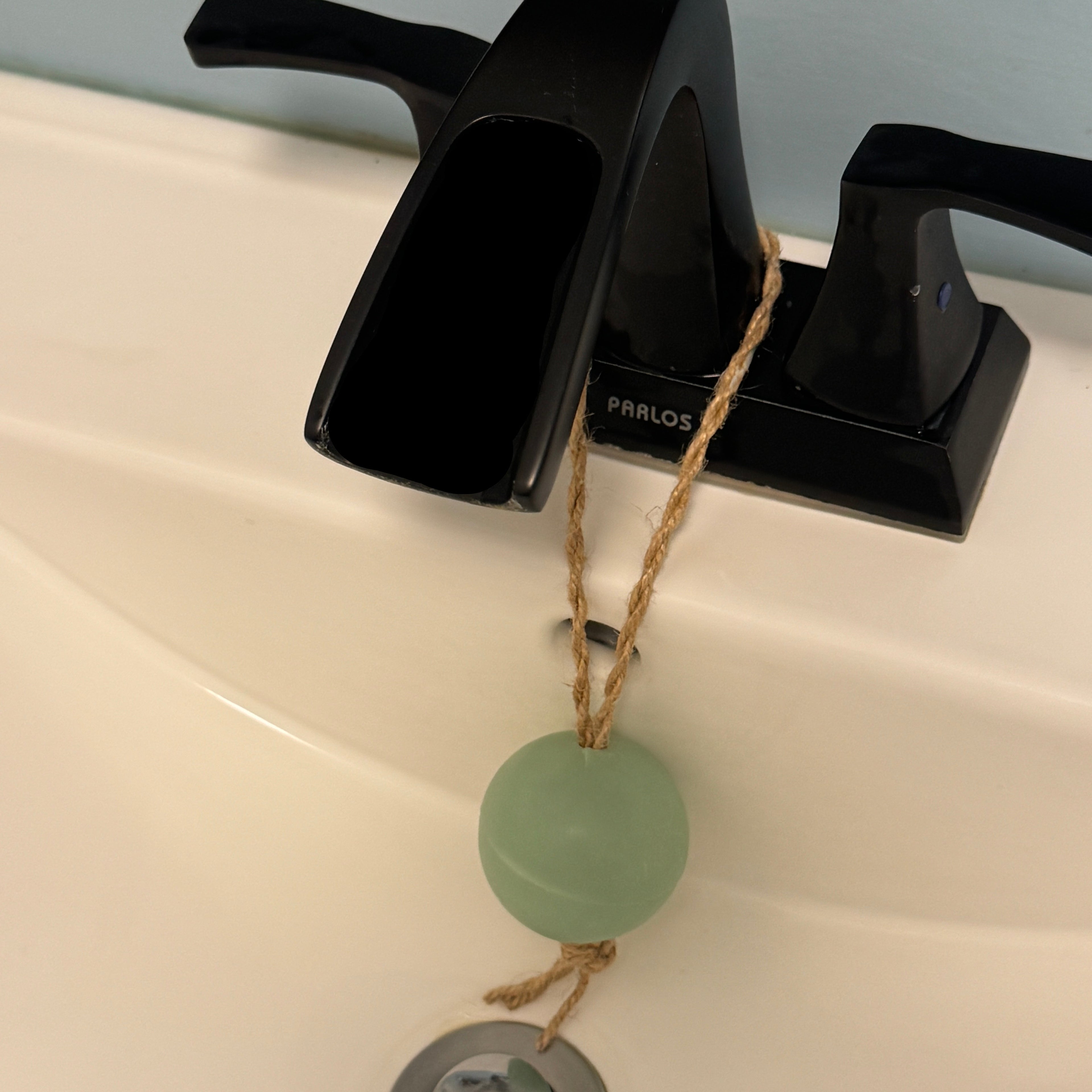 Black faucet with a green soap bar and string on a white sink
