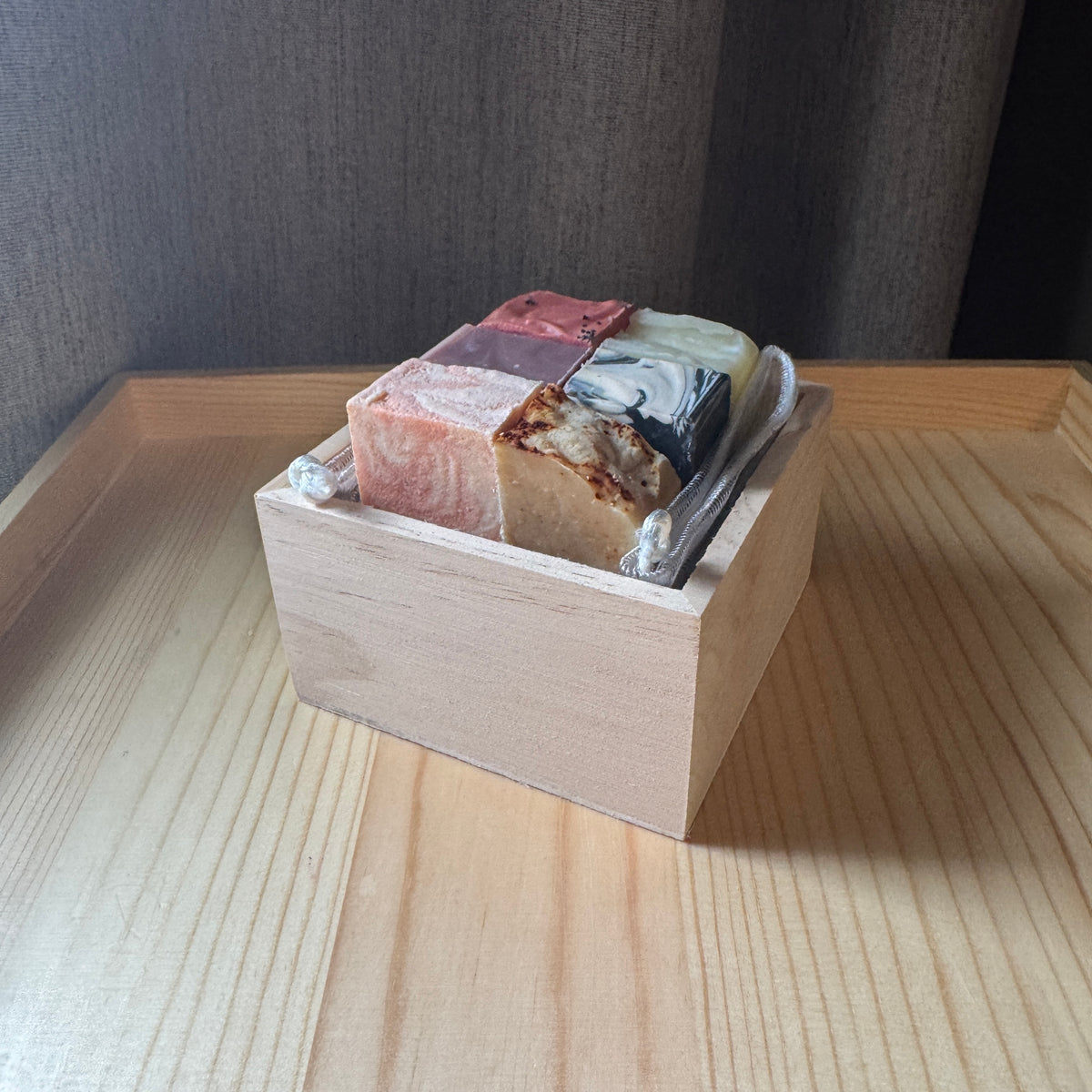 Assorted soap bars in a wooden box on a wooden surface with a dark background