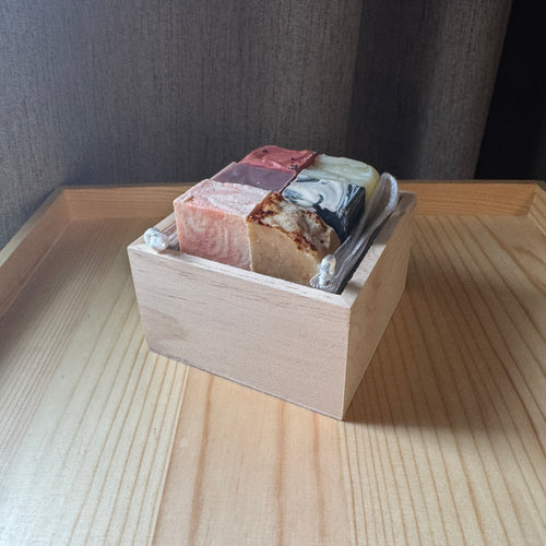 Assorted soap bars in a wooden box on a wooden surface with a dark background