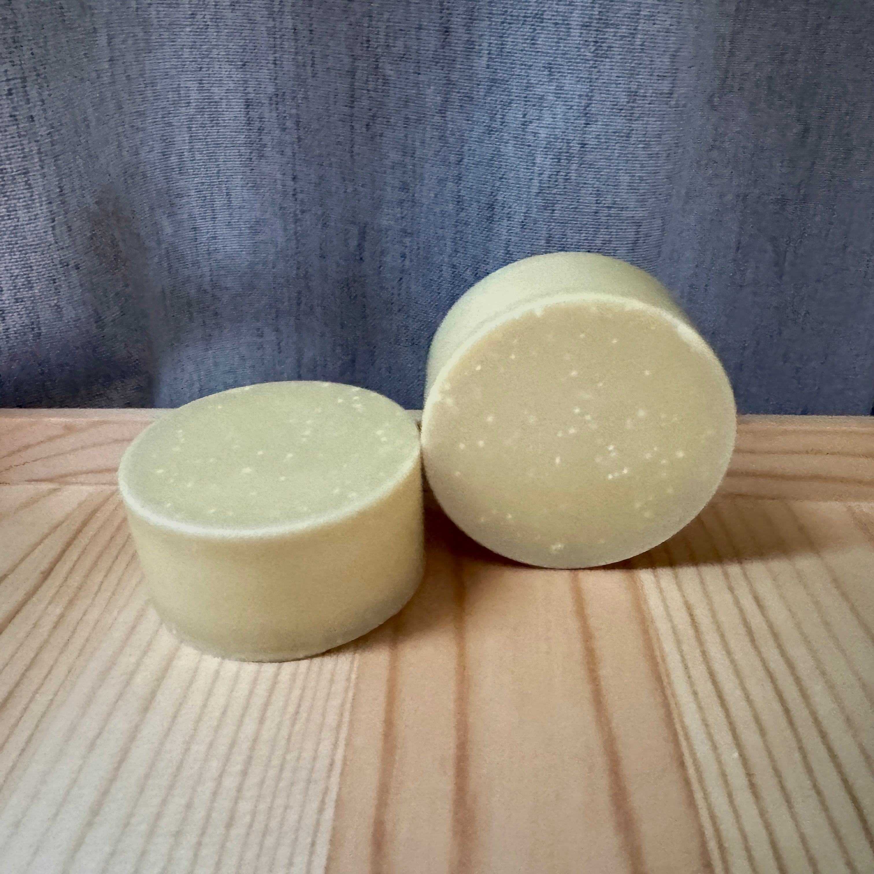 Two round, bars of soap on a wooden surface with a textured blue background