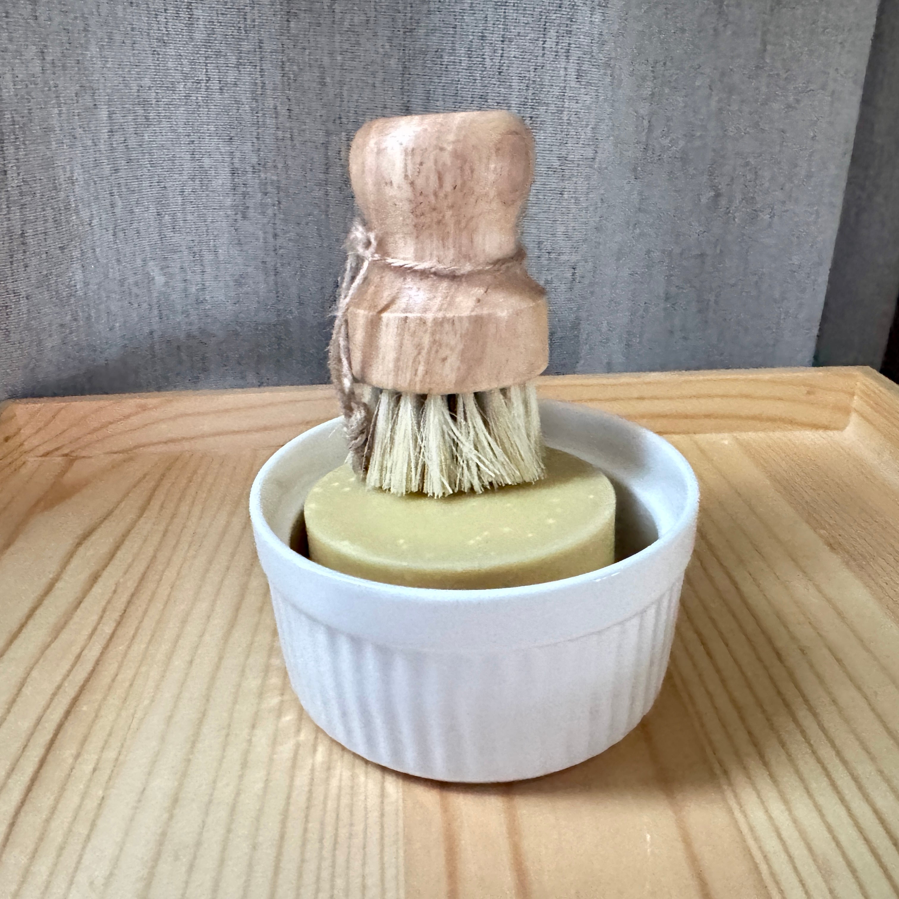Wooden dish brush with bristles in a white ceramic holder on a wooden surface.