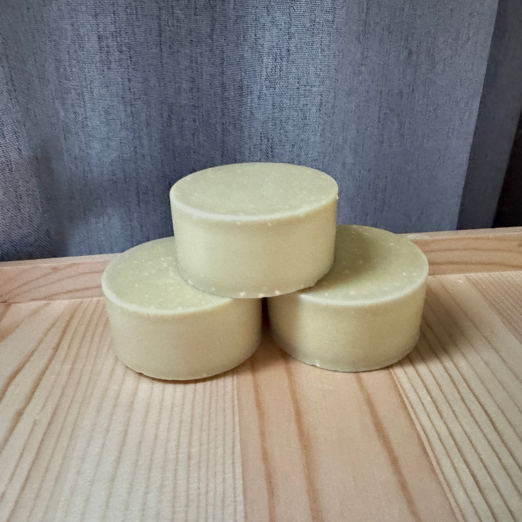 Three cylindrical beige soap bars stacked on a wooden surface with a gray textured background