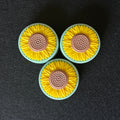 Three circular sunflower-shaped soaps arranged in a triangle on a dark textured background.