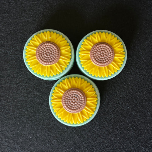 Three circular sunflower-shaped soaps arranged in a triangle on a dark textured background.