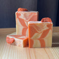 Three bars of soap with orange and beige swirls on a wooden surface.