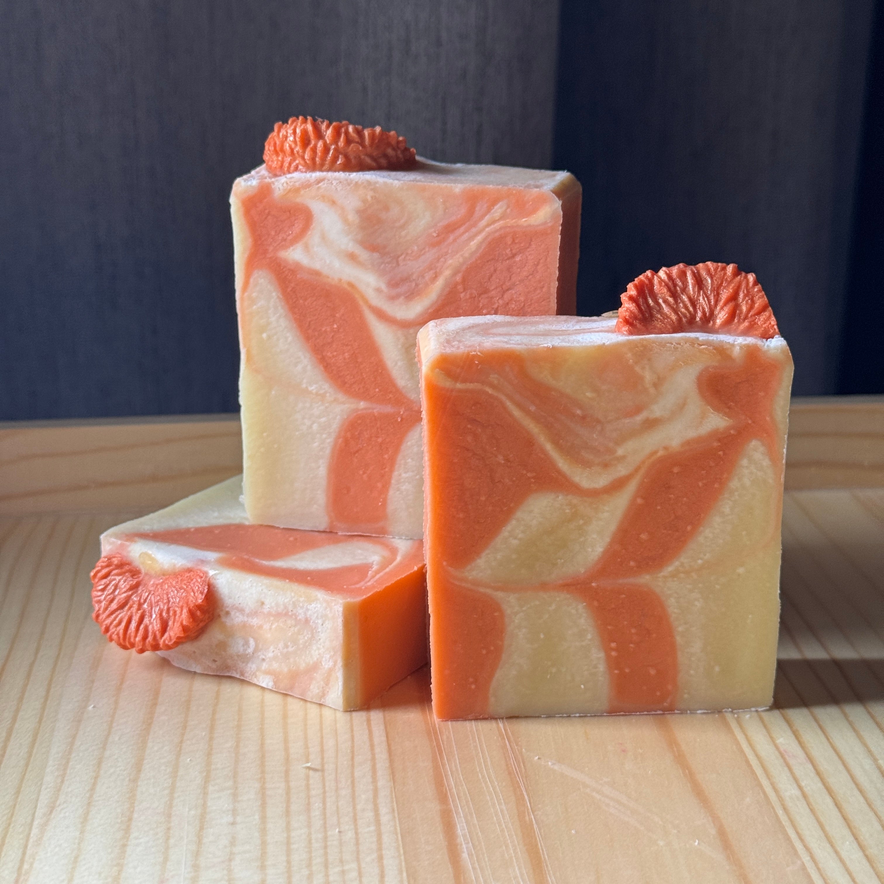 Three bars of soap with orange and beige swirls on a wooden surface.