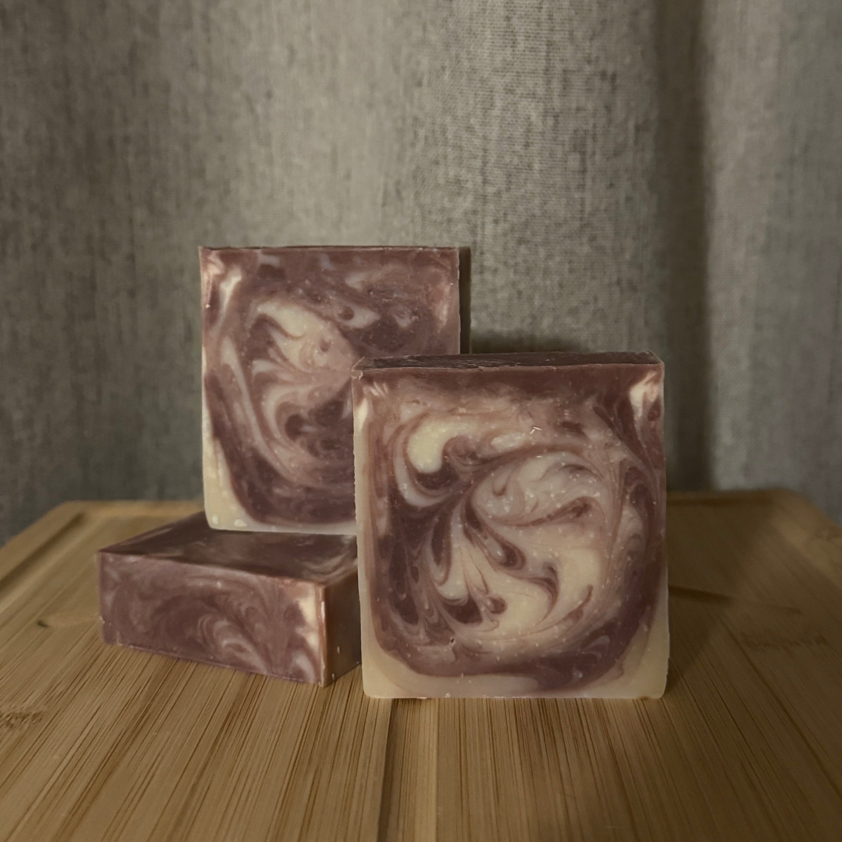 Three marbled soap bars on a wooden surface with a neutral background