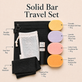 Solid Bar Travel Set laid out on a warm beige background with text labels identifying each item: a reusable black travel bag, soap saver bag, black washcloth, fragrance-free lip balm, and four solid bar soap bars in yellow, lavender, pink, and orange. The title 'Solid Bar Travel Set' appears at the top.