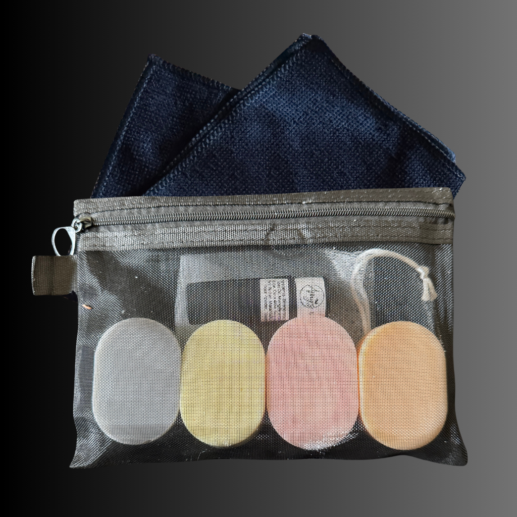 A black mesh bag with a zipper inside are 4 oval bars of soap plus one lip balm and a wash cloth and soap sack.