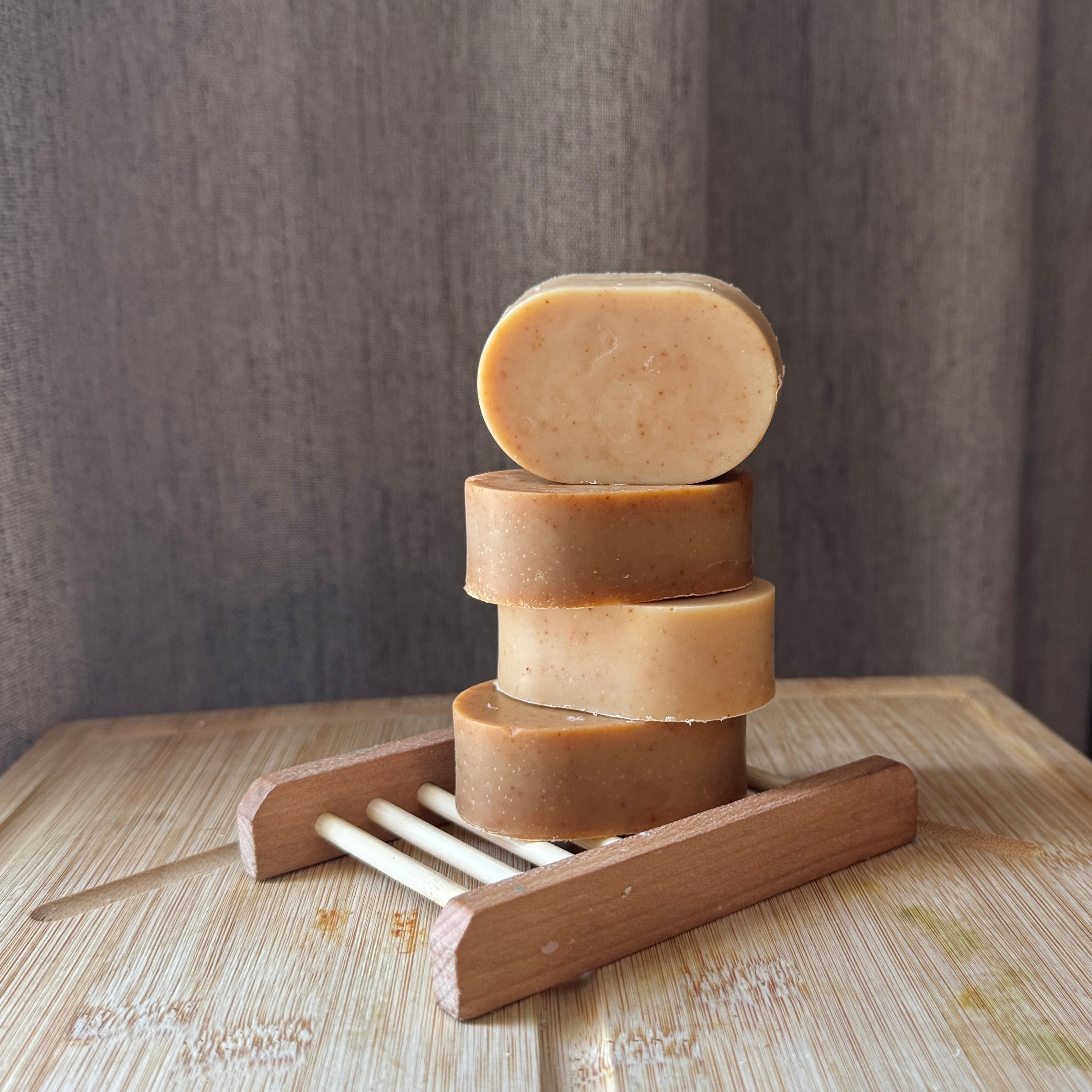 Stack of handmade soap bars on a wooden soap dish against a neutral background