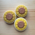 Three sunflower-shaped soaps with yellow petals and brown centers on a wooden surface.