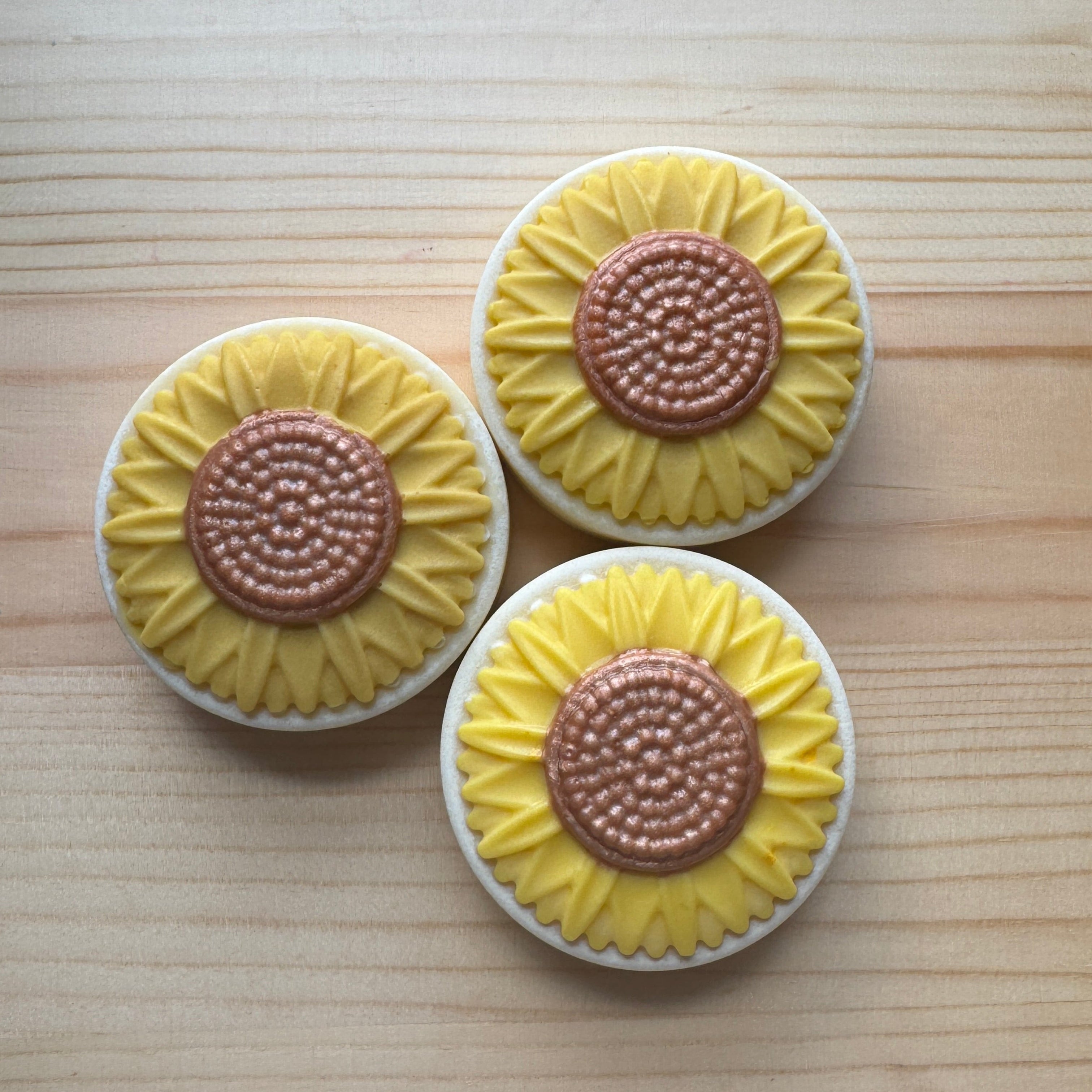 Three sunflower-shaped soaps with yellow petals and brown centers on a wooden surface.